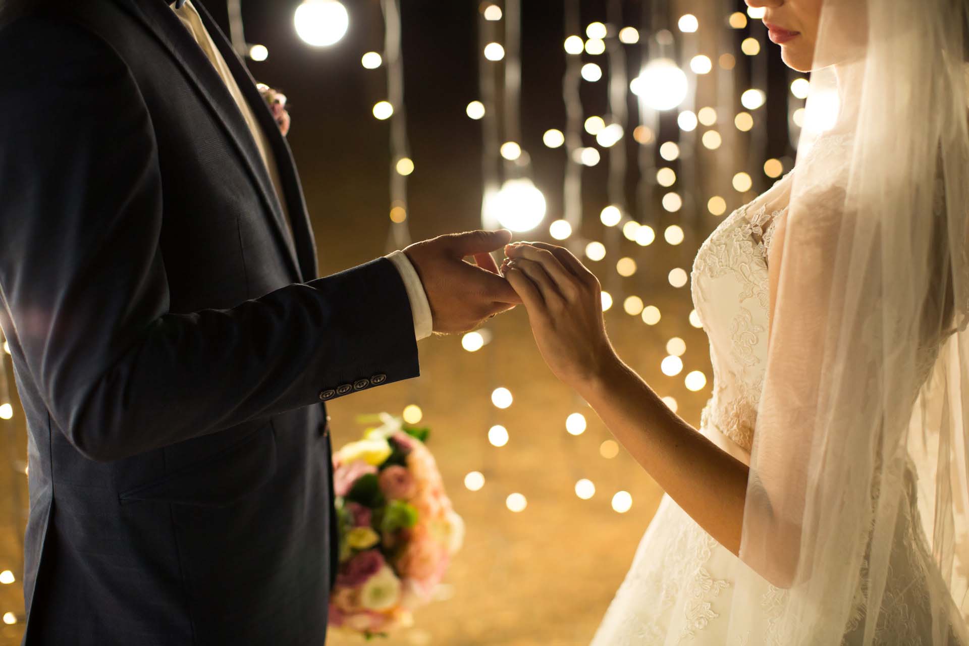 Evening wedding ceremony. The bride and groom holding hands on a Evening wedding ceremony. The bride and groom holding hands on a background of lights and lanterns.
