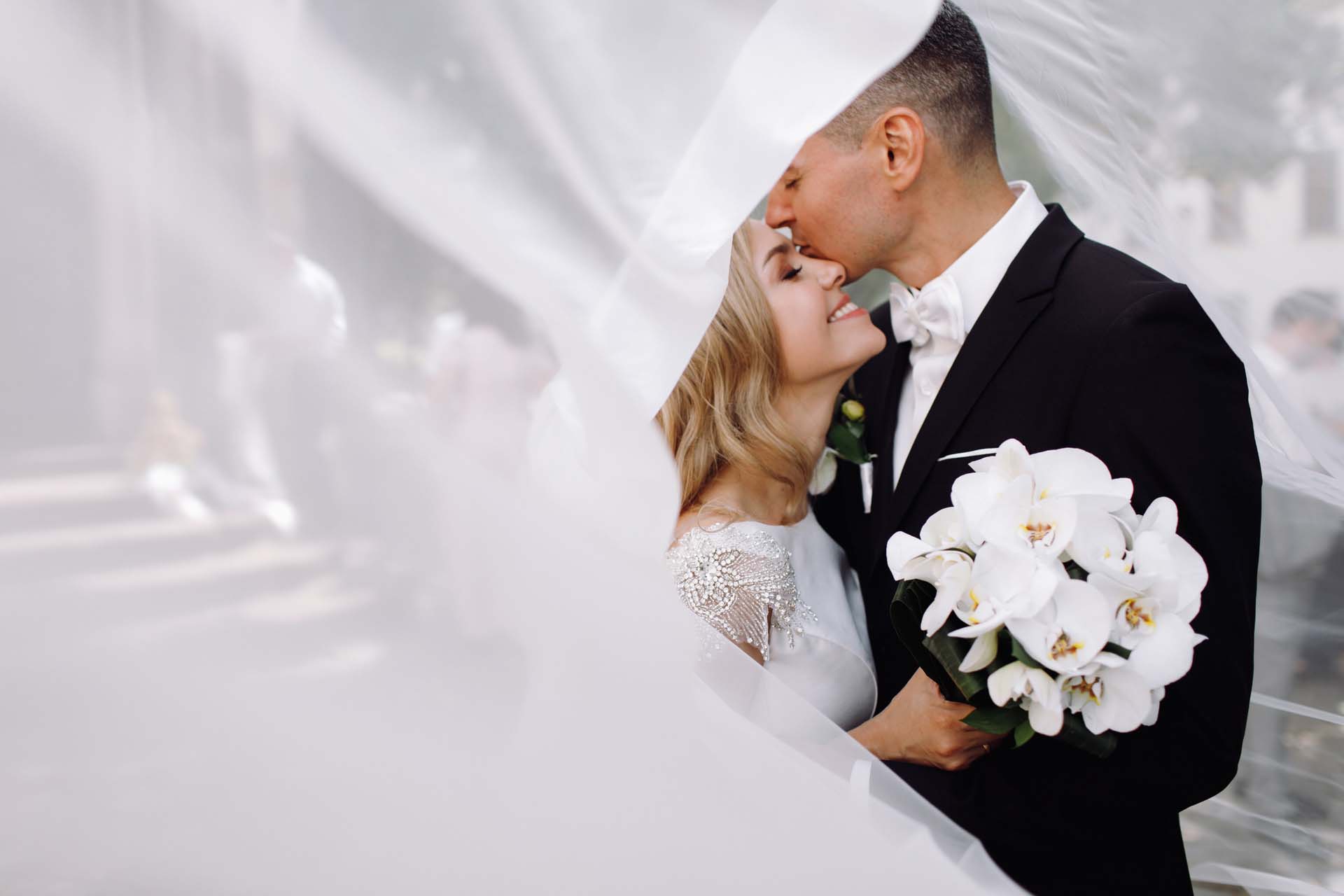Groom in black tuxedo hugs tender stunning bride while they stan Groom in black tuxedo hugs tender stunning bride while they stand on the street of old European town
